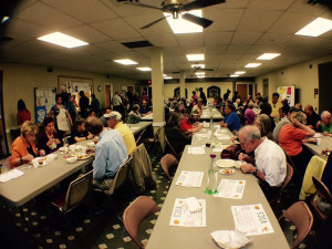 This is a photo of the church basement filled with folks eating dinner served by staff and residents of the WICS Home.